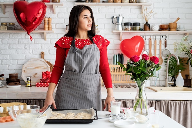 Woman in red dress and gray apron making valentine cookies at the kitchen