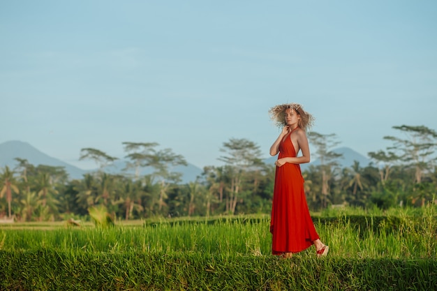 A woman in a red dress and hat walks in the rice fields in Bali 