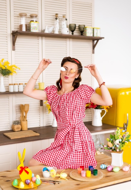 Foto donna in un vestito rosso è seduta in cucina decorata per le vacanze di pasqua la ragazza ha uova colorate decorative nelle sue mani