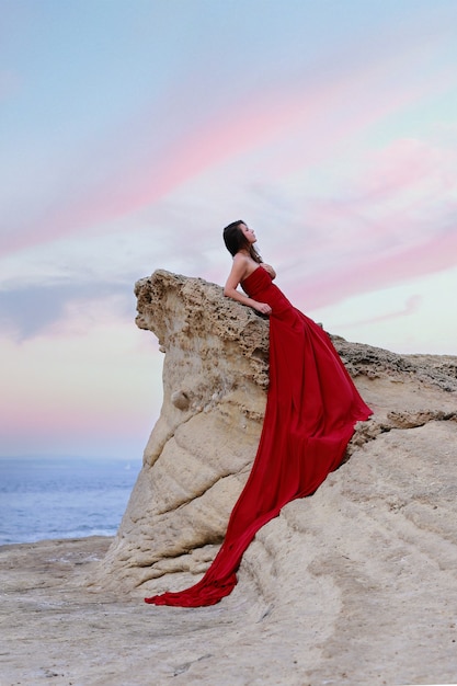 Woman in red dress long train next to sea.