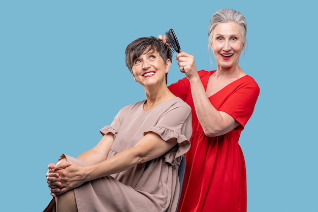 Woman in red dress making her friends hair and looking excited