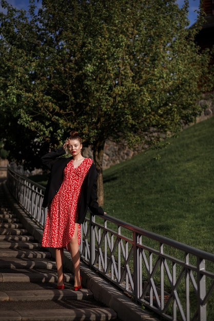 Woman in a red dress and a men's black jacket in the park in the summer.