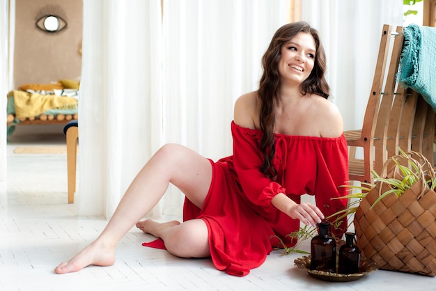 A woman in a red dress sits on the floor next to a plant