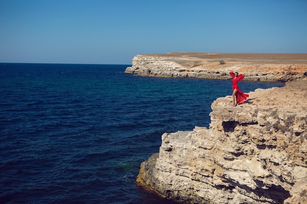 Женщина в красном платье стоит на скале у моря на скале летом