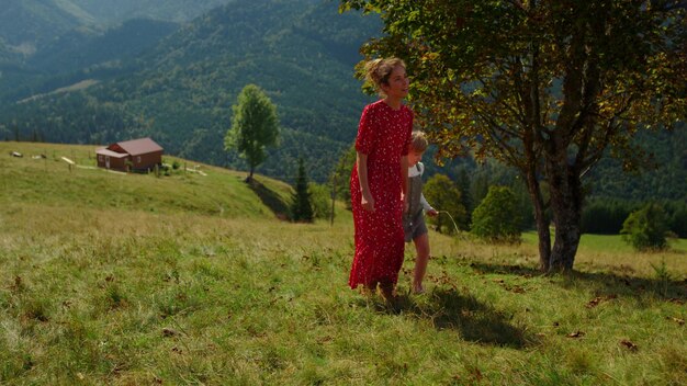 A woman in a red dress stands in a field with a mountain in the background.