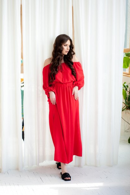 A woman in a red dress stands in front of a white curtain.