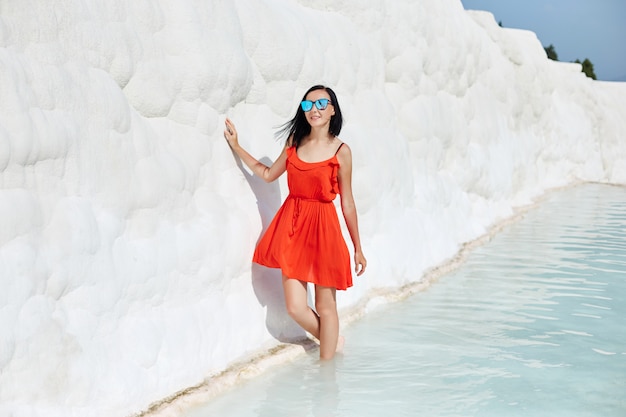 Woman in a red dress stands on white travertines. 