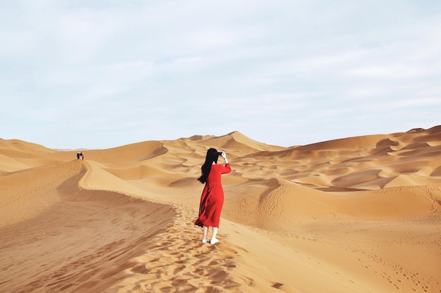 Woman in red dress taking photo in desert