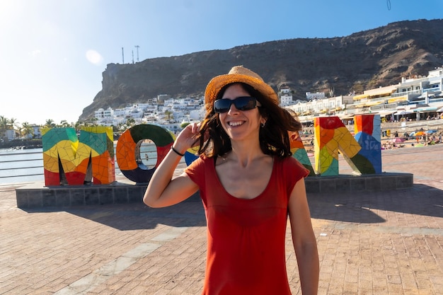 A woman in a red dress on the tourist sign in the coastal town of Mogan in the south of Gran Canaria Spain