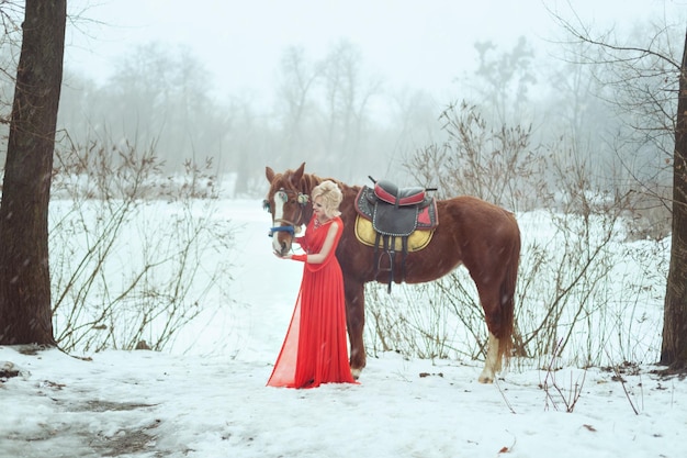 Woman in a red dress in the winter forest She strokes a horse