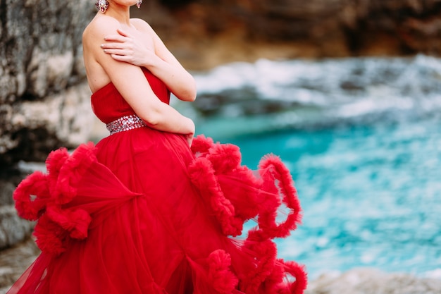 Woman in a red gown hugging herself on a rocky beach