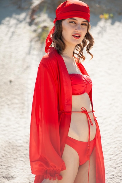 A woman in a red hat and a red hood stands in the sand.