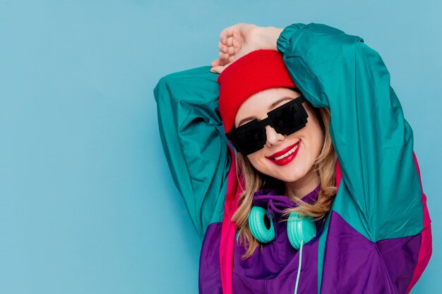 Donna con cappello rosso, occhiali da sole e tuta degli anni '90 con le cuffie