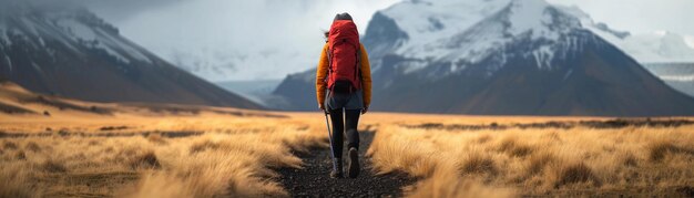 Photo a woman in a red jacket is walking in front of a mountain with a red backpack