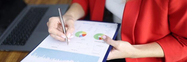 Woman in red jacket signs document on clipboard a table with colleague in office closeup. Marketing research market concept.