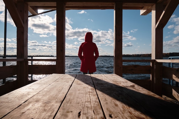 赤いジャケットを着た女性が木製の桟橋のテーブルに座って水を見ています