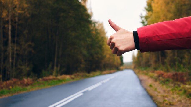 Photo a woman in a red jacket trying to stop a car on the forest road