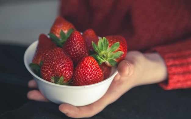 A woman in a red knitted sweater holds a plate of appetizing strawberries