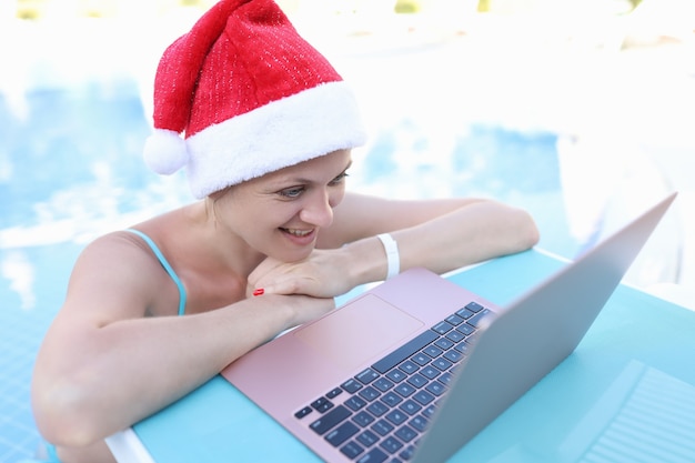 Woman in red santa claus hat looking at laptop on sunbed