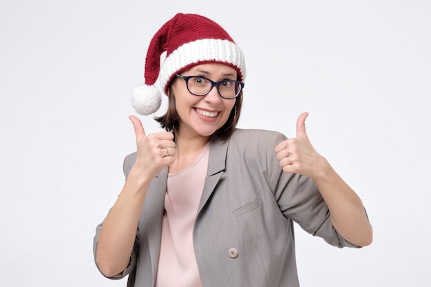 Женщина в красной шляпе Санта и очки показывает палец вверх, одобряя ваш выбор