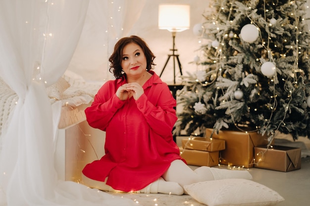 Женщина в красной рубашке в комнате, украшенной к Рождеству Домашняя новогодняя атмосфера