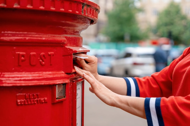 Woman in red short posting letters in red post box in England