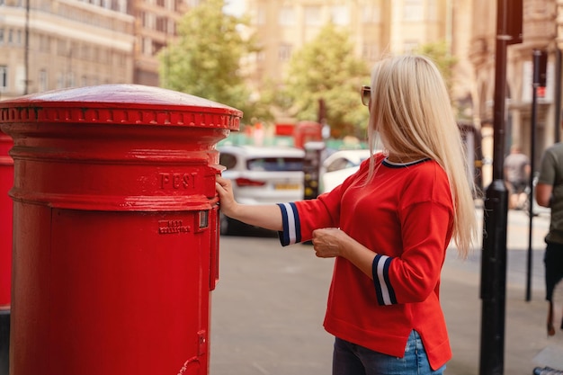 Photo woman in red short posting letters in red post box in england