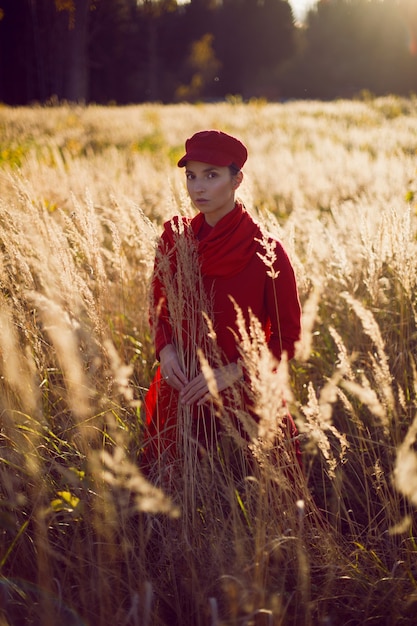 빨간 스웨터 모자와 스카프에 여자는 키가 큰 마른 풀밭에서 가을에 들판에 서