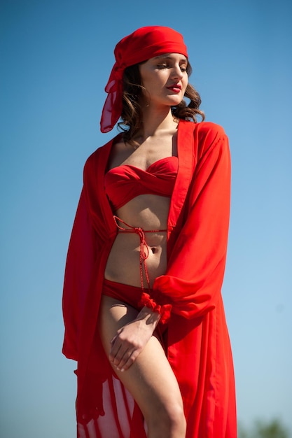 A woman in a red swimsuit and a red bow is standing in front of a blue sky.