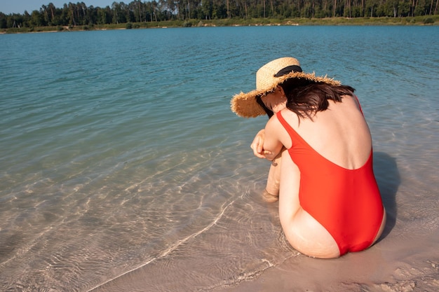 Woman in red swimsuit sitting at sandy beach summer sunbathing