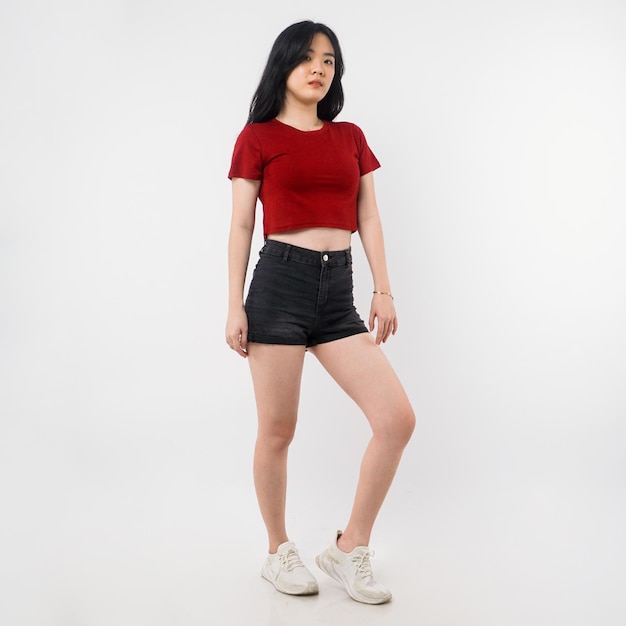 A woman in a red top and black shorts stands in front of a white background.