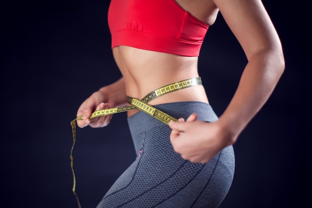 Woman in red top measuring her waist with meter. Sport, lifestyle and health concept