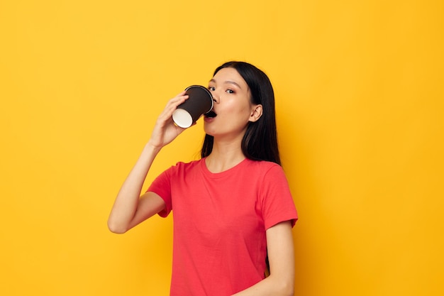 飲み物黄色の背景を持つ赤いTシャツガラスの女性