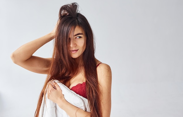 Woman in red underwear covering her body by towel in the studio against white background.