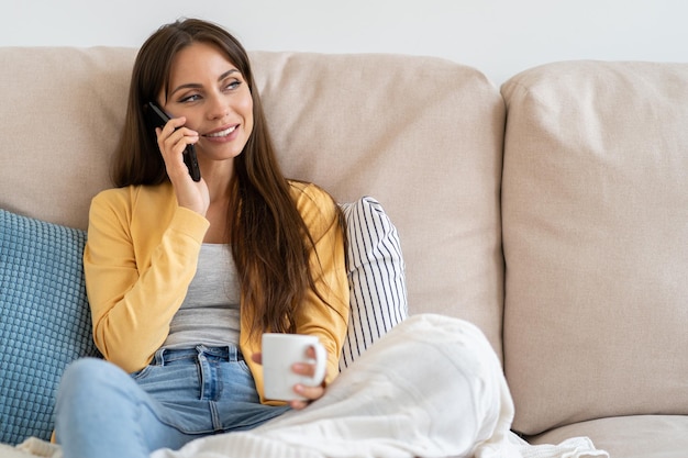 女性は自宅のソファに座って携帯電話で話しています