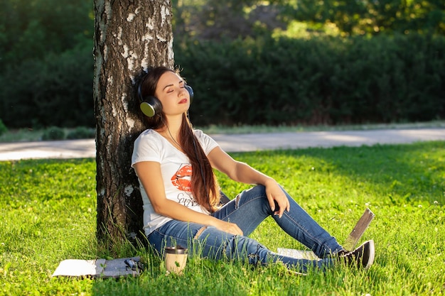 女性は公園の芝生の上に座って音楽を聴いてヘッドフォンでリラックス