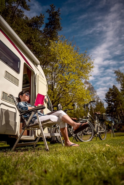 La donna si rilassa e legge un libro vicino al campeggio. vacanza in caravan. viaggio di vacanza in famiglia, viaggio di vacanza in camper.