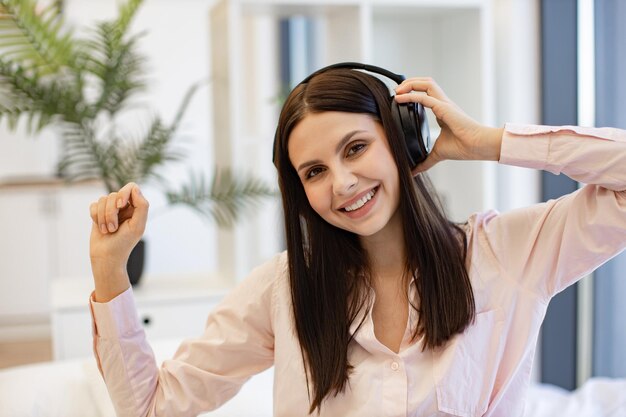 Woman relaxing on bed at home and using wireless headphones for listening songs