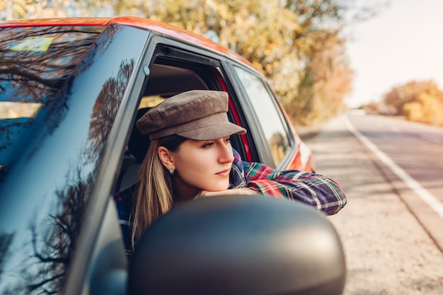 Woman relaxing in car. Driver looking out of autimobile window on autumn road.