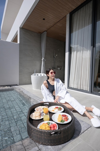 Woman relaxing and eating floating breakfast in the pool on luxury villa