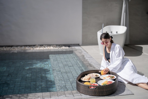 Woman relaxing and eating floating breakfast in the pool on luxury villa