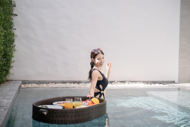 Woman relaxing and eating floating breakfast in the pool on luxury villa