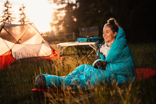 Woman relaxing and lie in a sleeping bag in the tent sunset\
camping in forest mountains landscape travel lifestyle camping\
summer travel outdoor adventure
