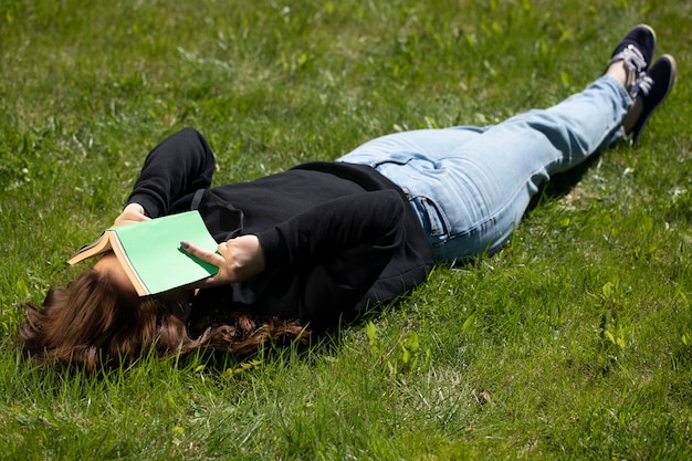 Photo woman relaxing in nature lying on green grass in park with open paper book on face