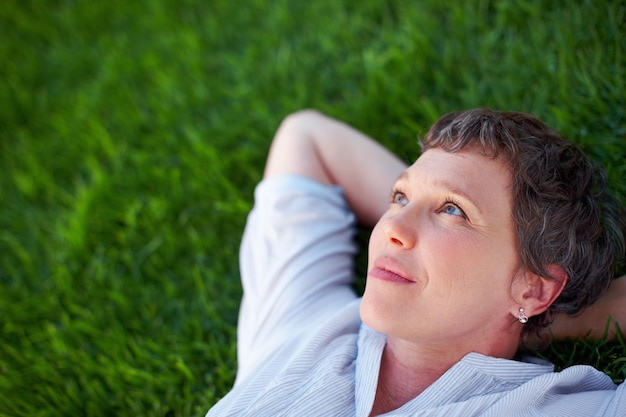 Woman relaxing outdoors Closeup of thoughtful mature woman relaxing while lying on grass