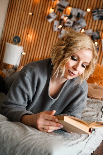 편안한 침대에 여자가 편안하고 책을 읽고-나무 벽과 조명 사진-배경을 흐리게-세로 사진