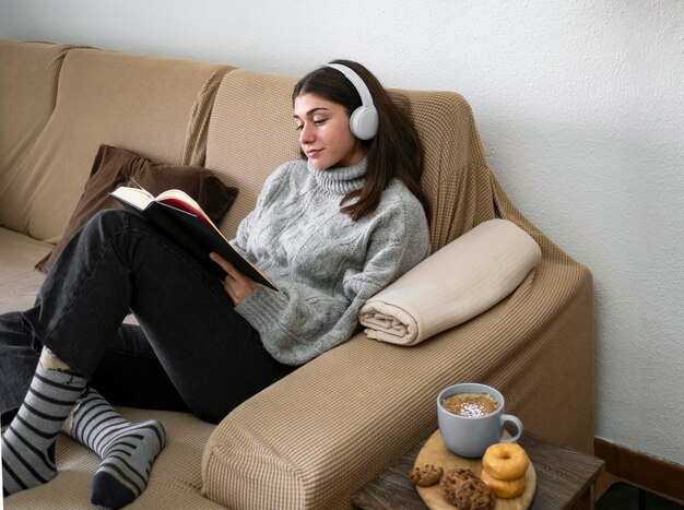 Woman relaxing reading a book and having a snack while lying on her back on a comfortable sofa