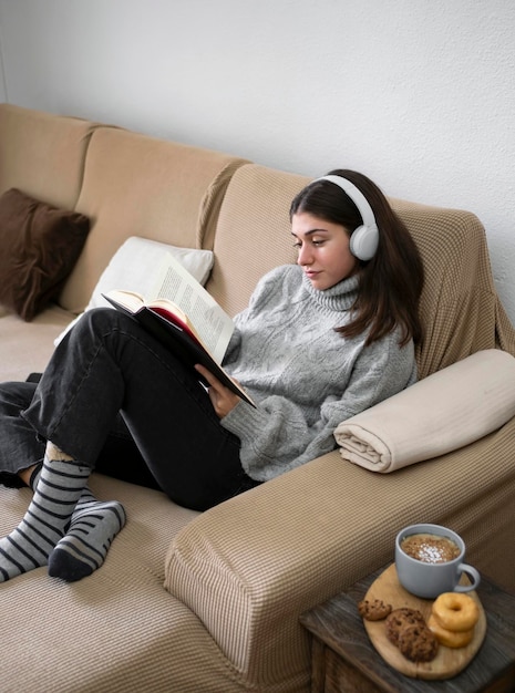 Woman relaxing reading a book and having a snack while lying on her back on a comfortable sofa