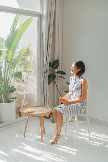 Woman relaxing and reading book near window in living room