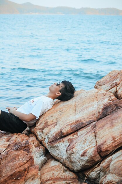 Foto donna che si rilassa sulla roccia vicino al mare